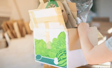 Eski karton kutuyu taşıyan ve depoda geri dönüşüme hazırlanan bir kadın..