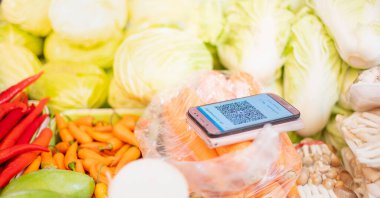 Alıcı, Covid-19 konseptiyle nakit ve el arasında temas kurmaktan kaçınmak için bir satıcıya ödeme yapmak üzere QR kodlu bir akıllı telefon hazırlıyor..