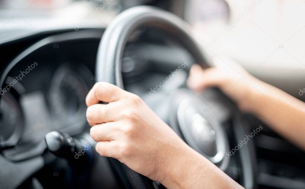 Close up view of woman hands holding steering wheel driving a car on the city road.