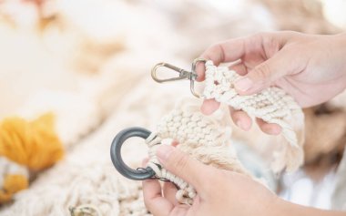 Kadın eli, detayı ve kusursuz ürünü kontrol etmek için paslanmaz anahtarlık ve ahşap askılı el yapımı Macrame bej iplik askısını seçiyor. Rahatlamak ya da satmak için bir el işi..
