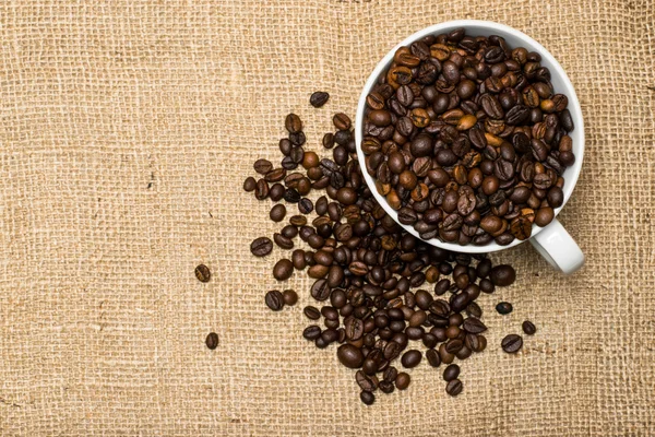 Cup full of coffee beans over cloth background — Stockfoto