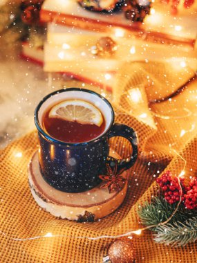 Mavi bardakta limonlu sıcak çay ahşap bir standın üzerinde duruyor, yanında bir ladin dalı, Noel oyuncakları ve bir çelenk var. Kar beyazdır. Sıcak çay iç. Noel ve Yeni Yıl. Noel içeceği.