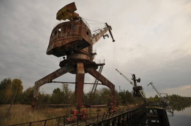 Pripyat hayalet kasabasındaki terk edilmiş kargo limanı, paslı eski rıhtım vinçleri, endüstriyel kıyamet sonrası manzara, Çernobil sınırlama bölgesinde sonbahar mevsimi, Ukrayna