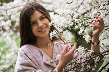 Çiçek açan kiraz ağacı olan esmer kadın. Çiçekli bahar bahçelerinde genç ve güzel bir kız portresi. Ellerinde beyaz narin çiçekler, bahar mevsimi, kremalı ve pastel elbiseler.