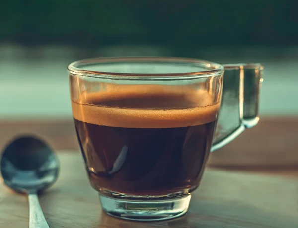 Espresso hot coffee in the morning on a cafe wood table with vintage light as background.