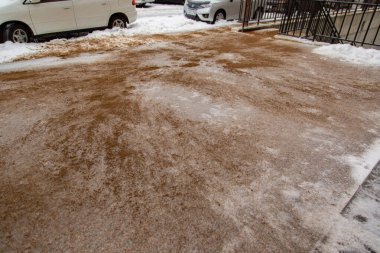 Kum, buzlu asfaltın üzerine serpilmiş, kar kaplı beton kiremitler insanların kaymaya karşı koyması için..