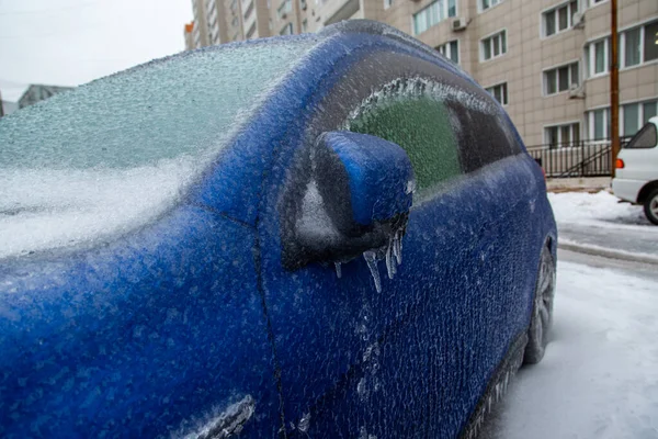 El coche azul está cubierto con una gruesa corteza de hielo, lluvia helada, en la ciudad. — Foto de Stock