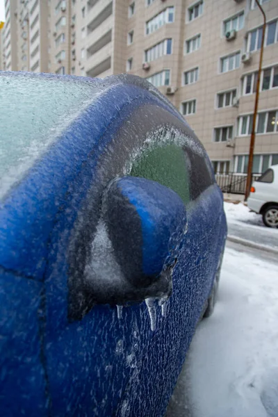 El coche azul está cubierto con una gruesa corteza de hielo, lluvia helada, en la ciudad. Foto vertical. — Foto de Stock