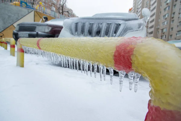 Žlutočervený plot v ledové kůře s rampouchy. Na pozadí SUV. — Stock fotografie