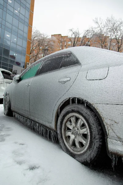 El coche gris de pasajeros estaba cubierto con una gruesa corteza de hielo después de la lluvia húmeda en la ciudad en invierno. — Foto de Stock