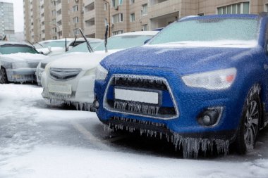 Mavi SUV ve diğer arabalar kışın yağan yağmurdan dolayı donmuş ve buzlu olarak şehirde dururlar. Buz engelliyor..