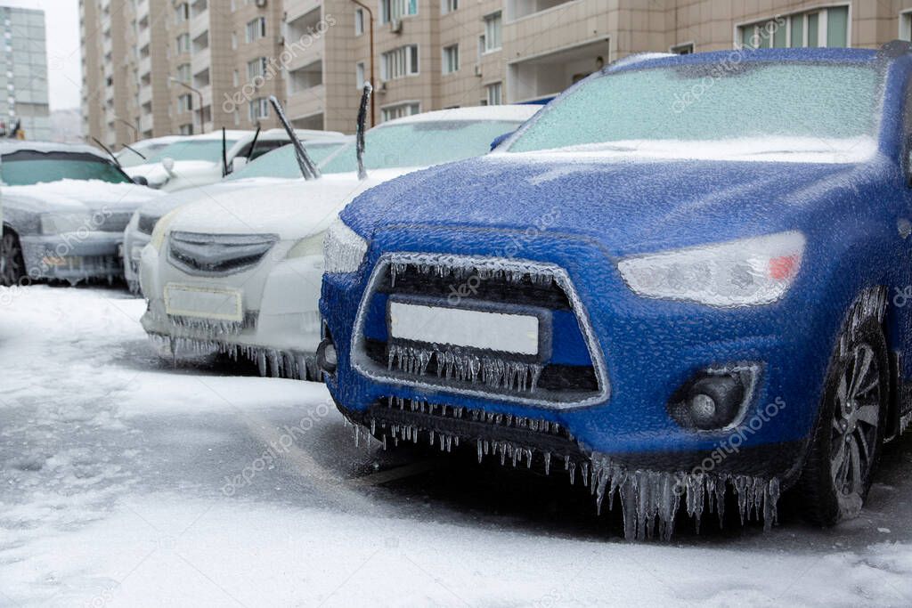 The blue SUV and other cars stand in the city frozen and icy from the rain in winter. Blocked by ice.