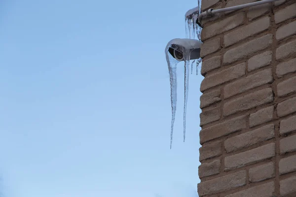 Eine an einer Ziegelwand befestigte Überwachungskamera ist stark vereist, Eiszapfen hängen herunter.. — Stockfoto