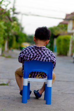 Yalnız çocuğun otur beton yollarda plastik sandalye