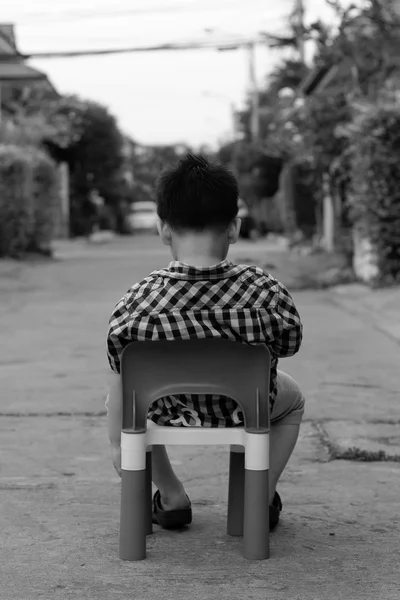 Один мальчик сидит на пластиковом стуле на бетонной дороге — стоковое фото