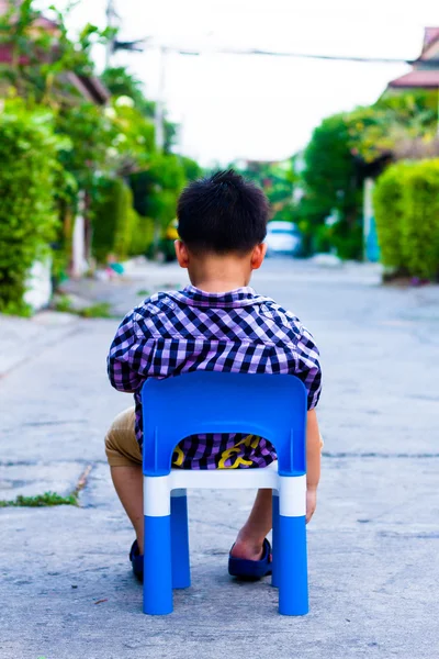 Один мальчик сидит на пластиковом стуле на бетонной дороге — стоковое фото