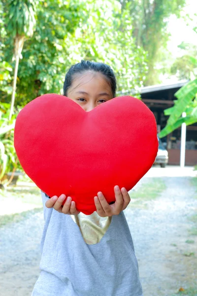 Χαριτωμένο κορίτσι χαμογελά κρατώντας μια κόκκινη καρδιά παιχνίδι — Φωτογραφία Αρχείου