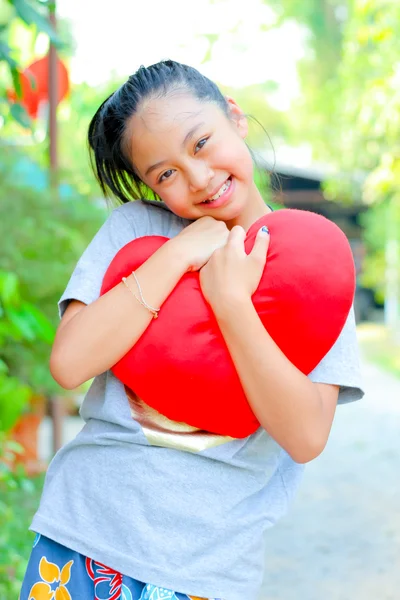 Cute girl smiling holding a red heart toy — Stock Photo, Image