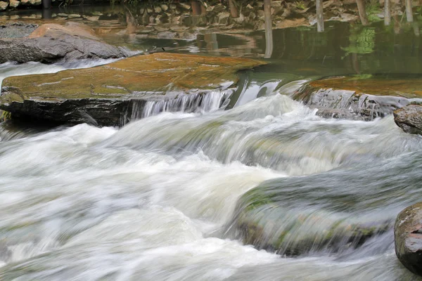 Водопад течет над камнем в реке — стоковое фото