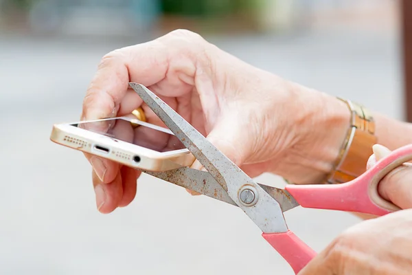 Den gamle mannen handen håller saxen och klippa mobiltelefon. — Stockfoto