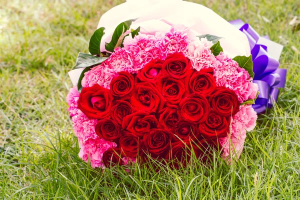 Röda rosor och rosa nejlika på grass grön — Stockfoto