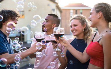 Gün batımında terasta bir kadeh şarapla kadeh kaldıran dört genç çocuk.