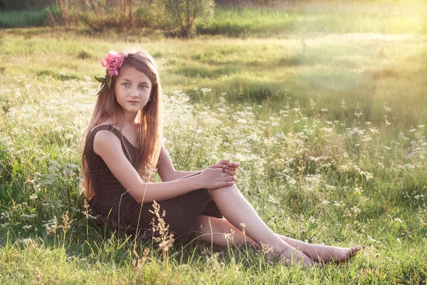 Девушка с пионом в волосах сидит на поле и смотрит на — стоковое фото