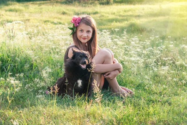 Flicka med pion i hennes hår och svart hund — Stockfoto