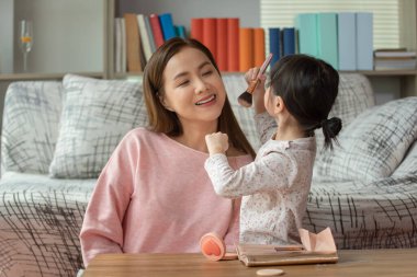 Mutlu çocuk, küçük Asyalı kız annesiyle makyaj yapıyor, sevgi dolu aile kavramı.