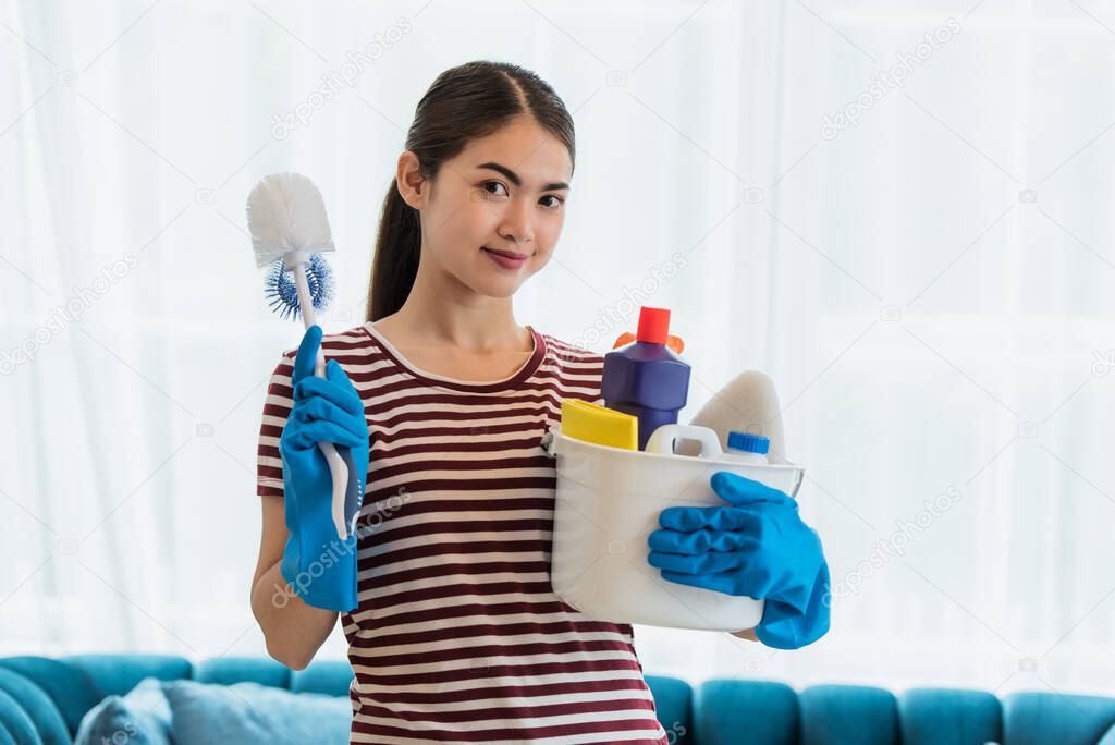 Happy young Asian housewife wearing gloves and holding basket with cleaners and brushes, cleaning and washing concept