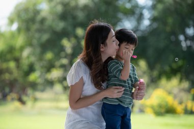 Mutlu Asyalı aile parkta sabun köpüğüyle oynayan anne ve oğlu eğleniyor.