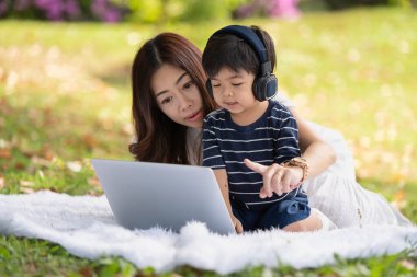 Mutlu Asyalı aile parkta dizüstü bilgisayar kullanarak eğleniyor.