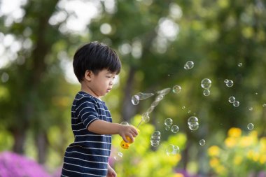 Mutlu Asyalı çocuk parkta sabun köpüğüyle oynarken eğleniyor.