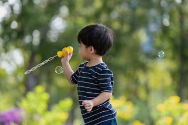 Mutlu Asyalı çocuk parkta sabun köpüğüyle oynarken eğleniyor.