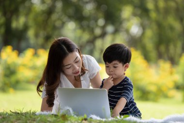 Mutlu Asyalı aile parkta dizüstü bilgisayar kullanarak eğleniyor.