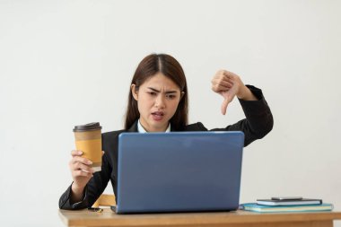 Stresli Asyalı iş kadını dizüstü bilgisayarda çalışıyor ve ofisinde baş parmağını gösteriyor, iş kavramı, olumsuz duygular.