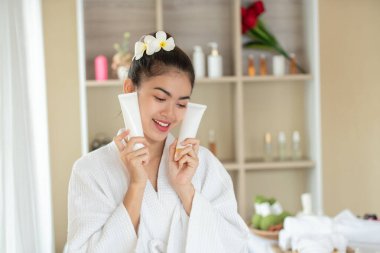 Güzel Asyalı kadın beyaz kozmetik tüpü tutuyor ve sunuyor.