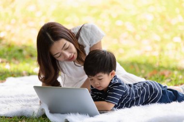 Mutlu Asyalı aile parkta dizüstü bilgisayar kullanarak eğleniyor.