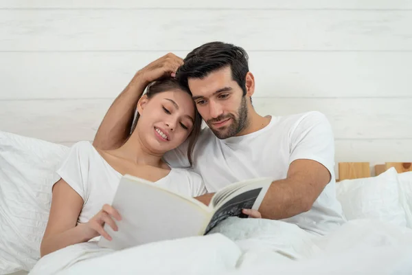 Happy young relaxed couple read a book together and laughing while lying on the bed