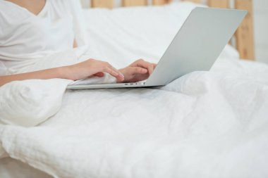 Yatağa uzanmış, yatak odasında bilgisayar kullanan bir kadın.