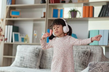 Mutlu Asyalı çocuk kulaklıkla müzik dinlerken ve bir odada dans ederken eğleniyor. Aktif eğlence ve yaşam tarzı kavramı.