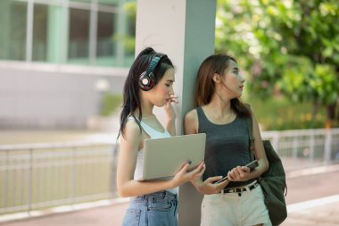 Kampüste dizüstü bilgisayarla okuyan ve dijital tablet, eğitim konsepti kullanan Asyalı genç öğrencilerin portresi