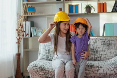 Asyalı anne ve çocuk kızı sarı mühendis kaskı, eğitim ve meslek konsepti takıyor.
