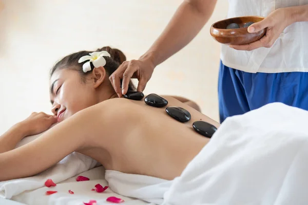Young Asian woman lying down on massage bed with traditional hot stones along the spine in spa salon, enjoying and relaxing time