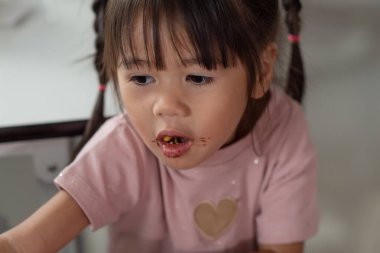 Happy little Asian child eating dessert at home kid has dirty mouth with chocolate