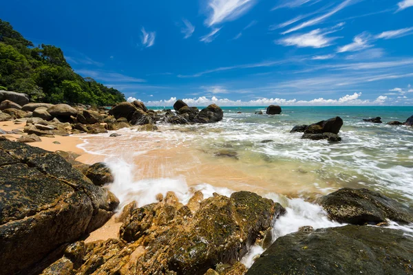 Морские волны плети линии удара скалы на пляже под голубым небом — стоковое фото