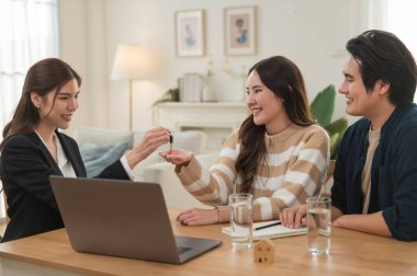 Emlakçı ev anahtarlarını müşteriye veriyor. Asyalı kadın emlakçı ev modeliyle aynı masada otururken alıcıya anahtarları veriyor. Gayrimenkul, yeni mülk alımı, ipotek konsepti