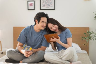 Asyalı bir çift dijital tablet kullanarak ve ellerinde küçük bir alışveriş arabası tutarak online alışveriş yapıyor. E-ticaret, finansal planlama, dijital yaşam tarzı, modern ilişki kavramı.