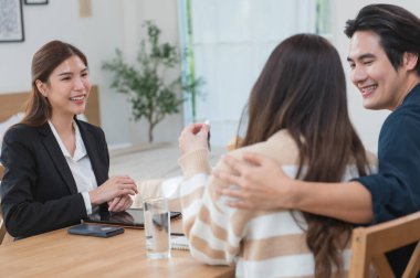 Asyalı finans danışmanı ofisteki genç çifte yeni proje yatırımını açıklıyor. Emlakçı aileyle ipotek seçeneklerini tartışıyor. Finans danışmanıyla ipotek kredisi danışmanlığı.