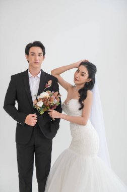 Asyalı çift evleniyor, mutlu Asyalı çift düğün kıyafetleri içinde, gelin güzel beyaz bir gelinlik ve damatla klasik bir takım elbise giyiyor, ikisi de çekici ve aşık görünüyorlar.